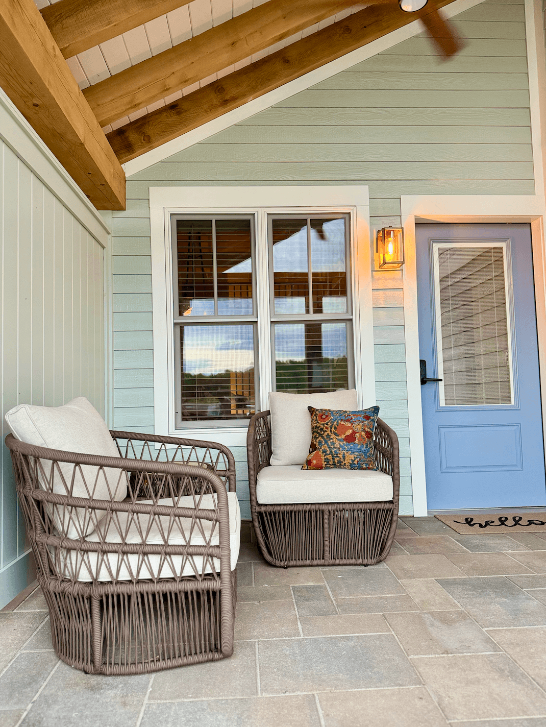 A welcoming porch with light blue siding features two woven outdoor armchairs with cream cushions and a pastel blue door.