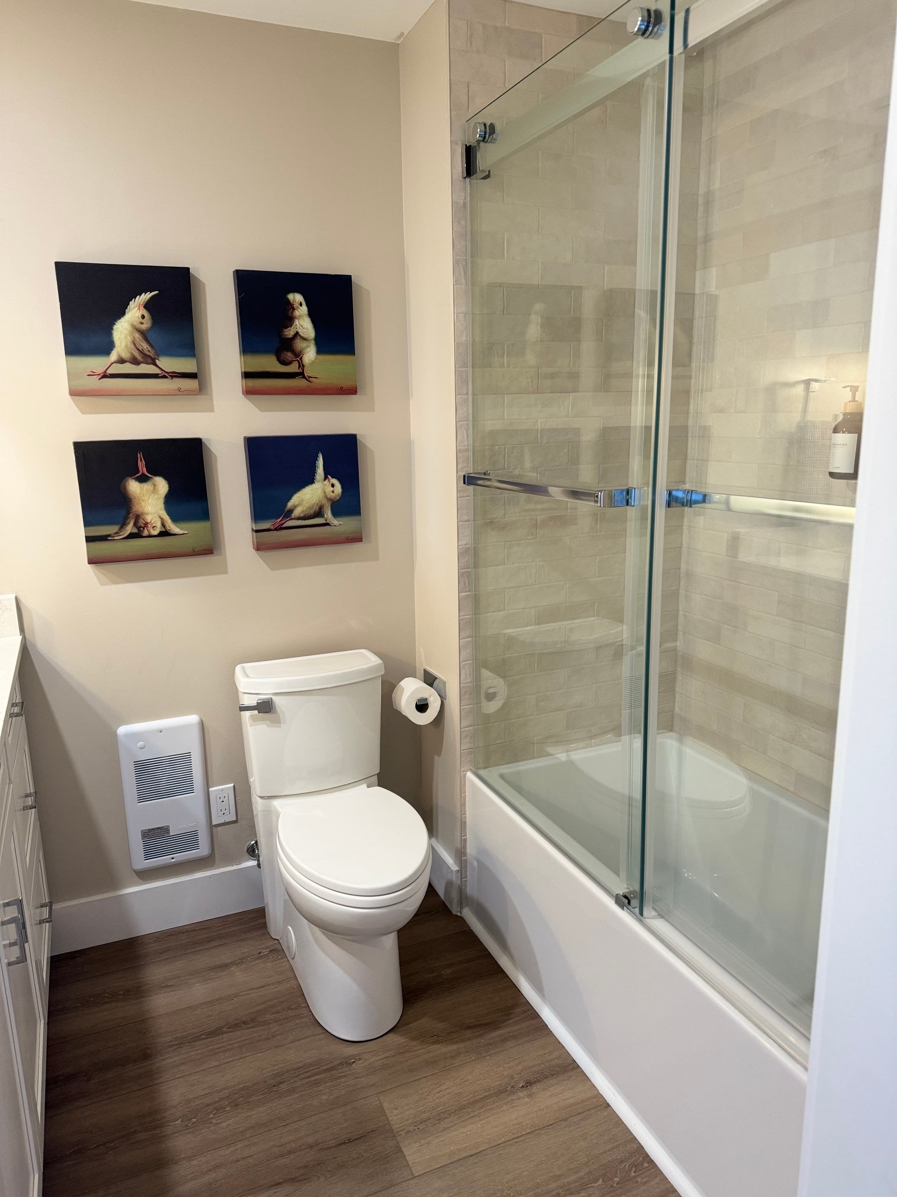 A modern bathroom featuring a white toilet, soaking tub/shower with a glass door, and whimsical rabbit artwork on the wall.
