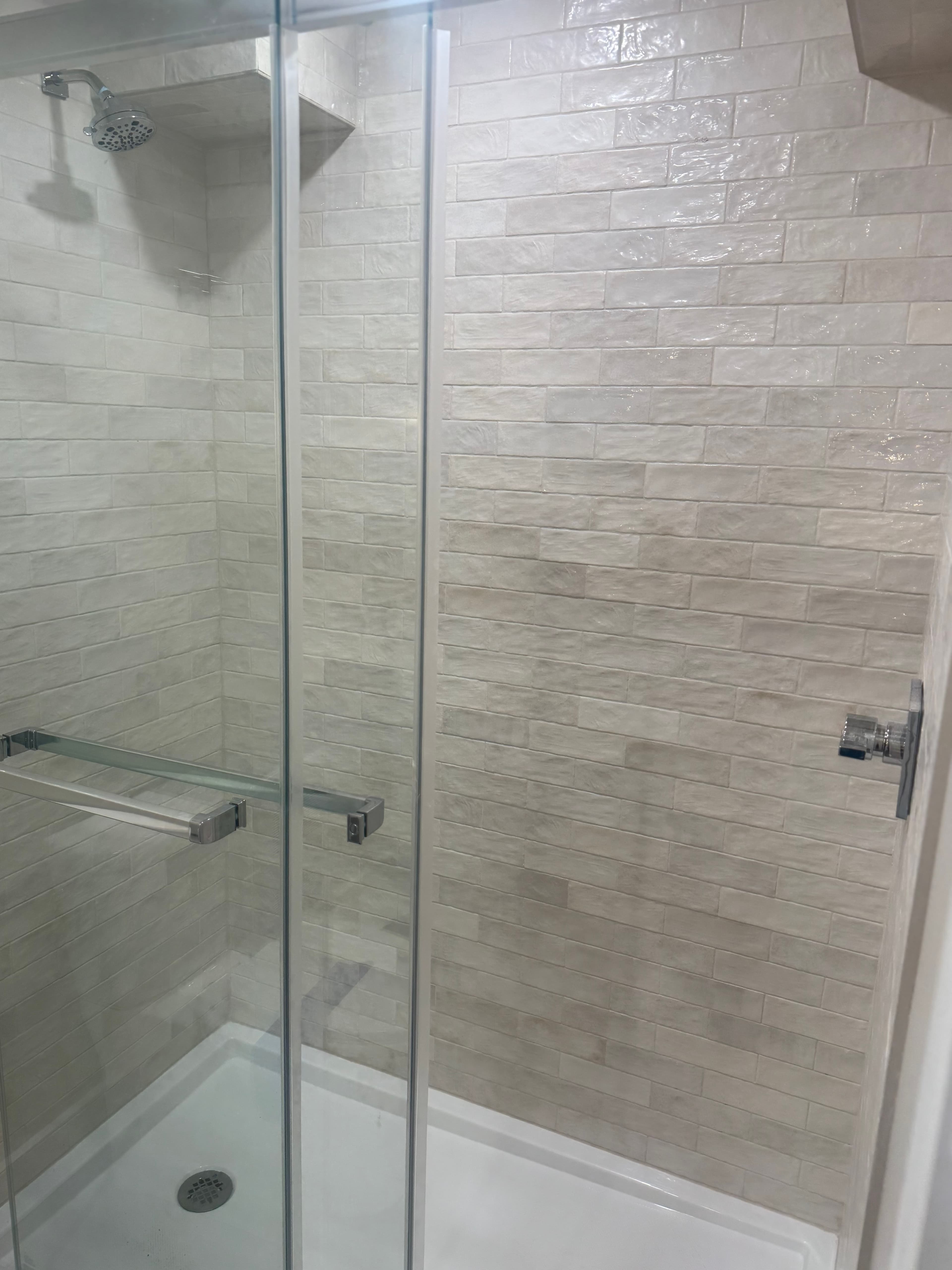 A modern walk-in shower with a glass enclosure and light tiled walls.