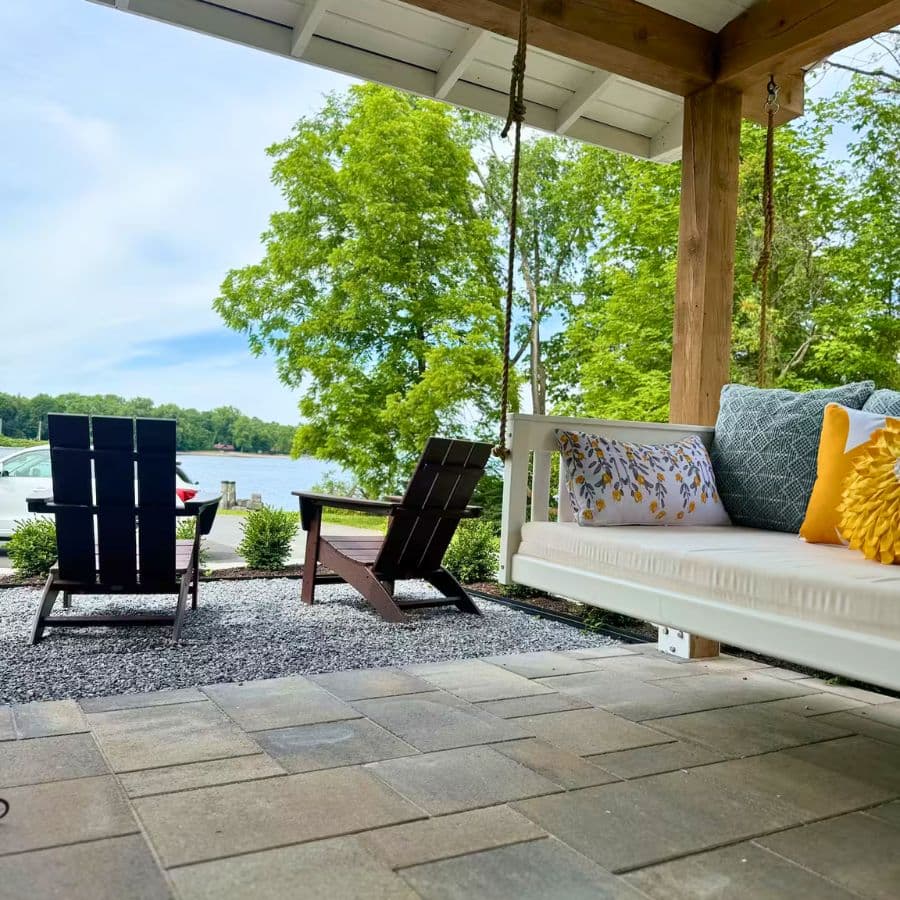 A cozy outdoor seating area by a lake, featuring two chairs and a swing surrounded by greenery.