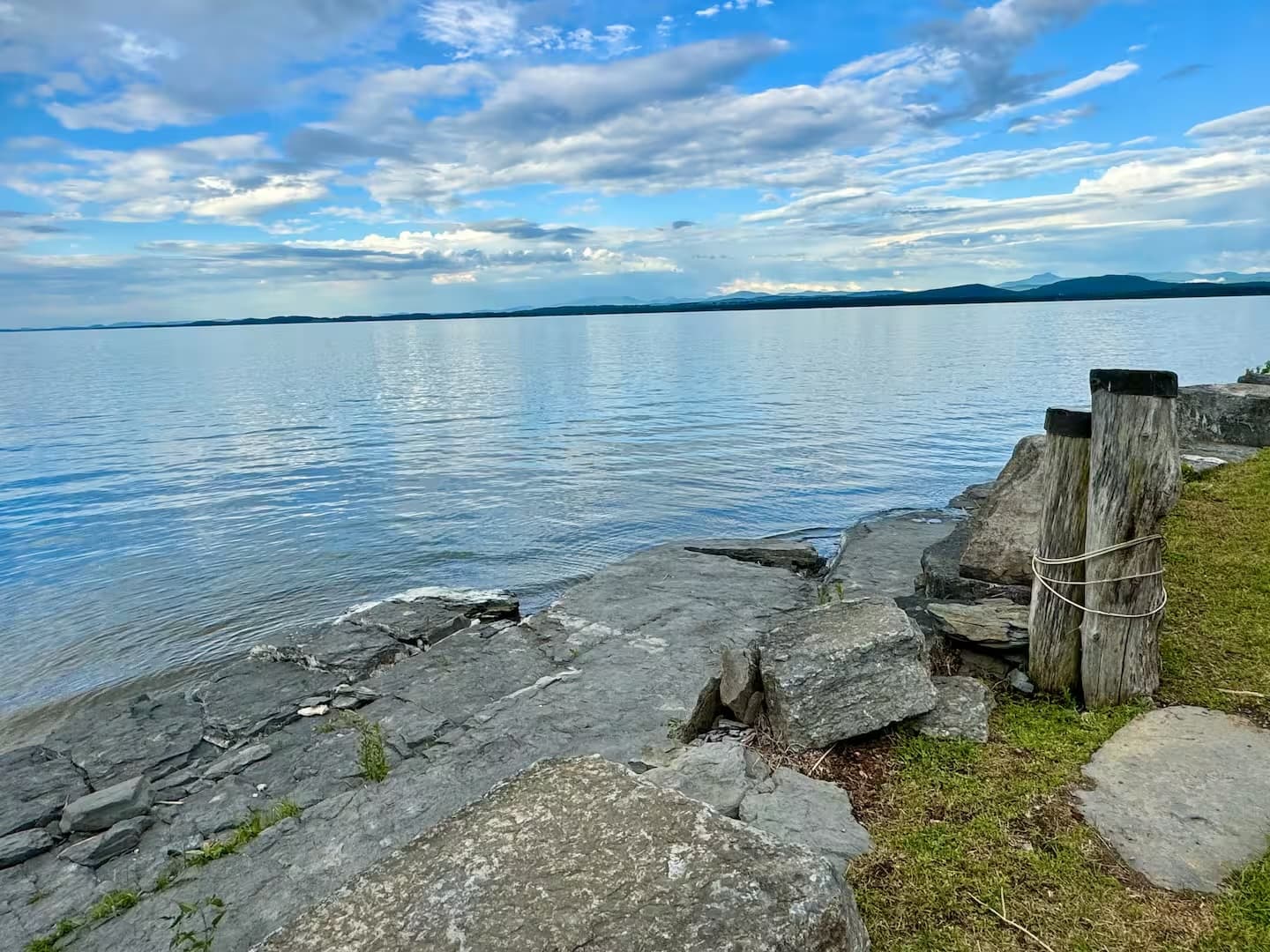 Calm water reflecting a blue sky, with rocky shorelines and wooden posts in the foreground.