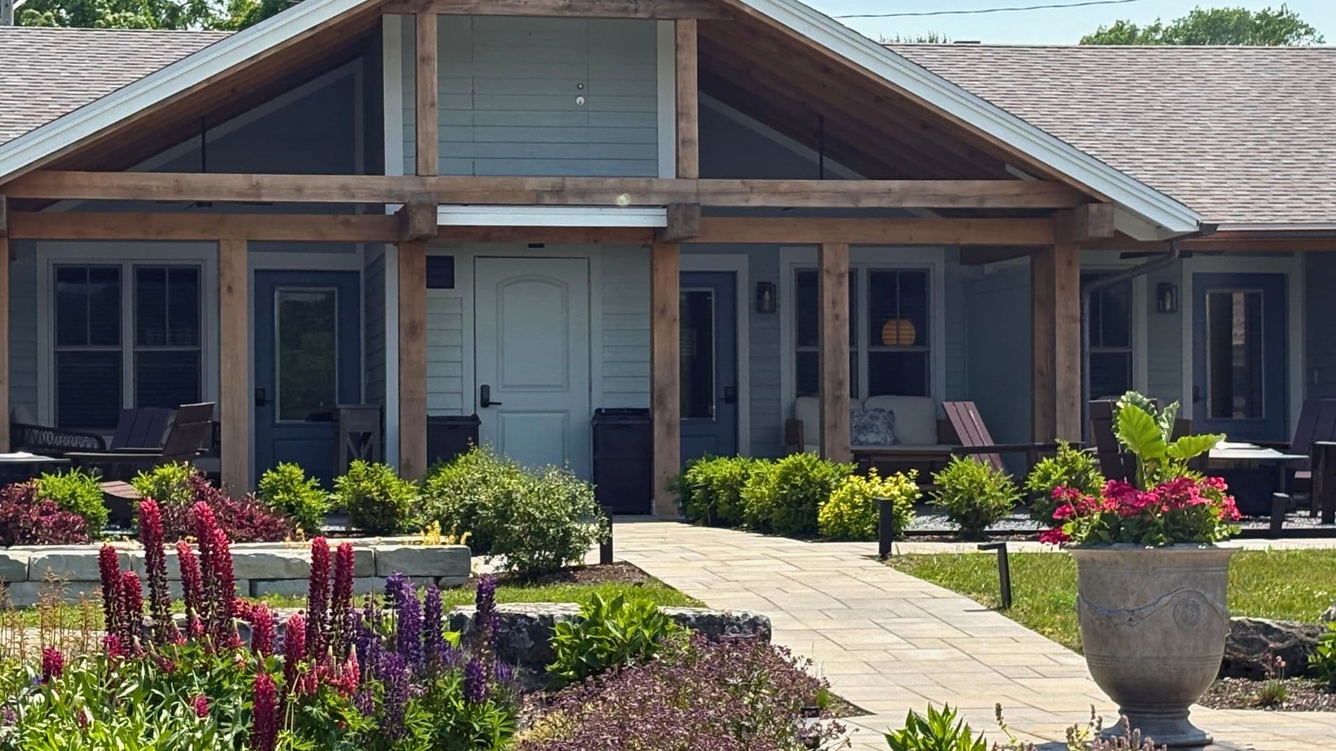 A modern house with a wooden porch surrounded by colorful flowerbeds and greenery.