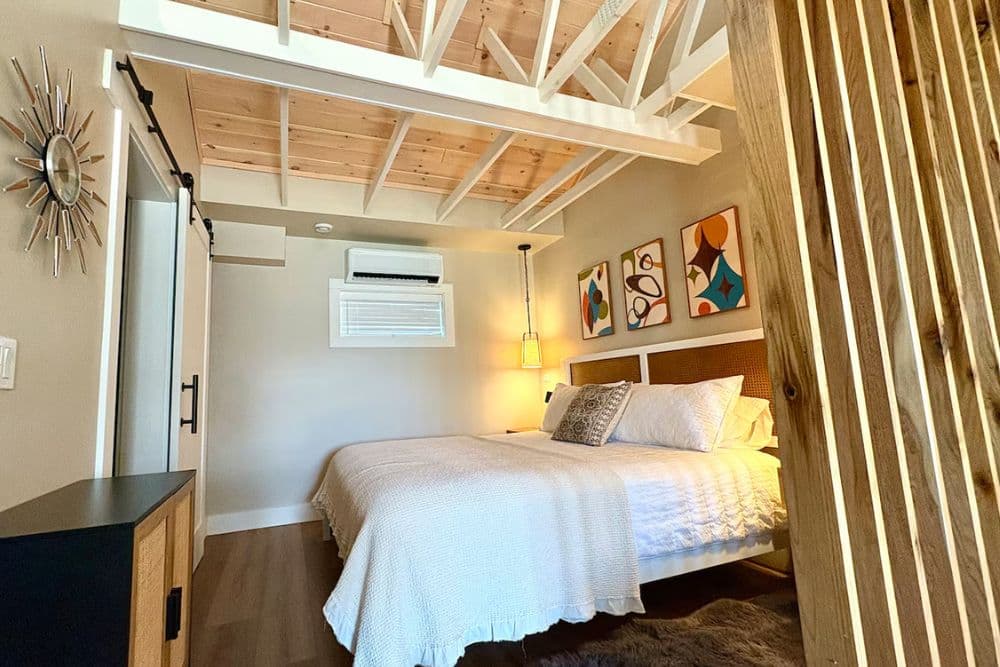 A cozy bedroom featuring a large bed, wooden ceiling beams, and modern artwork on the walls.