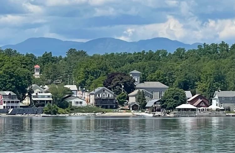 A scenic lakeside view of a small town with various houses and mountains in the background.