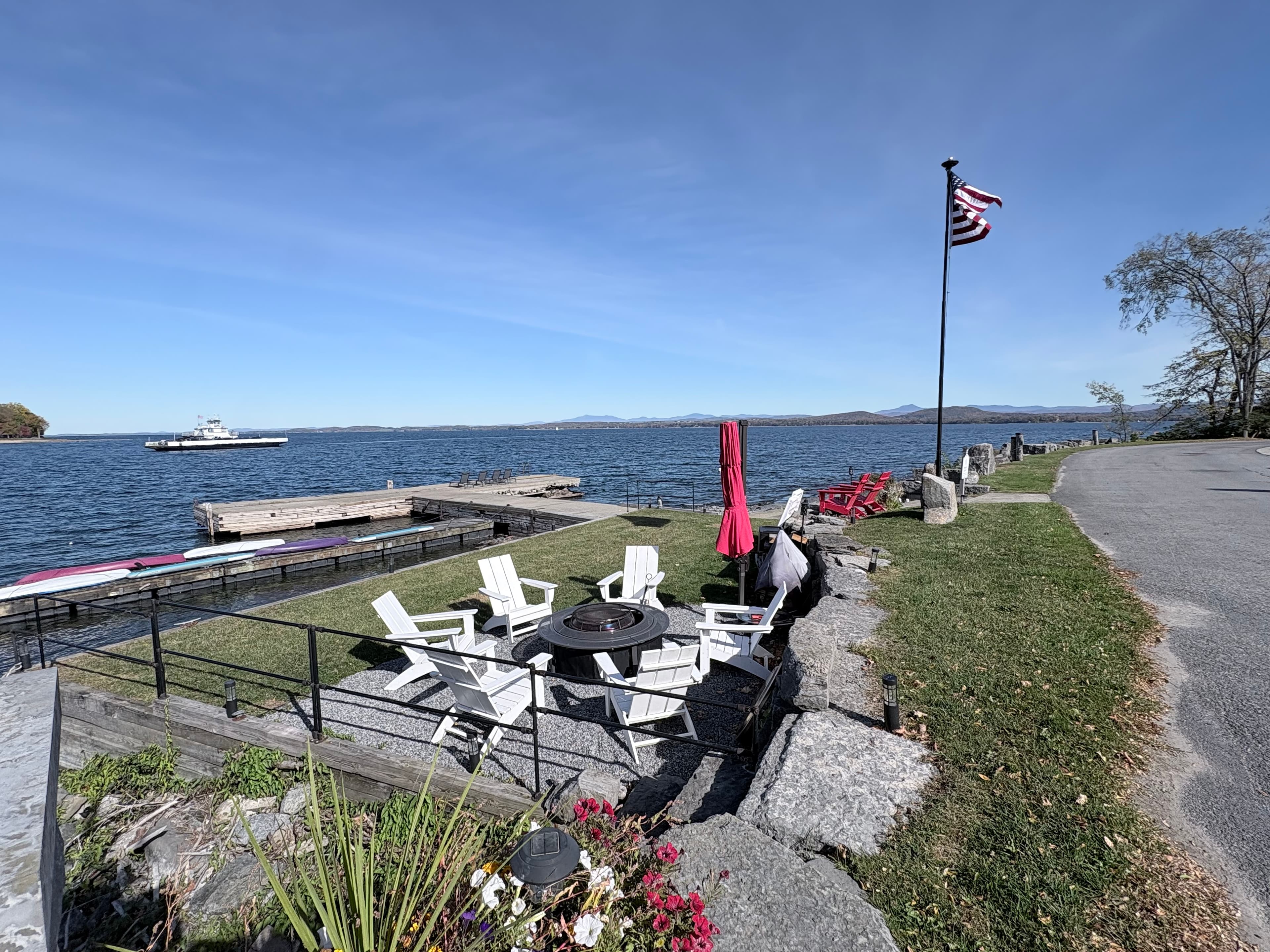 A scenic view of a lakeside with seating arrangements, a flagpole, and a ferry on the water.