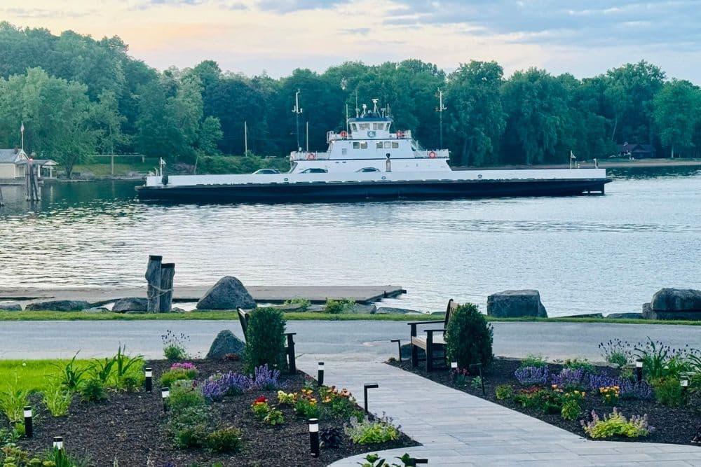 A ferryboat navigates across a calm river, surrounded by lush greenery.