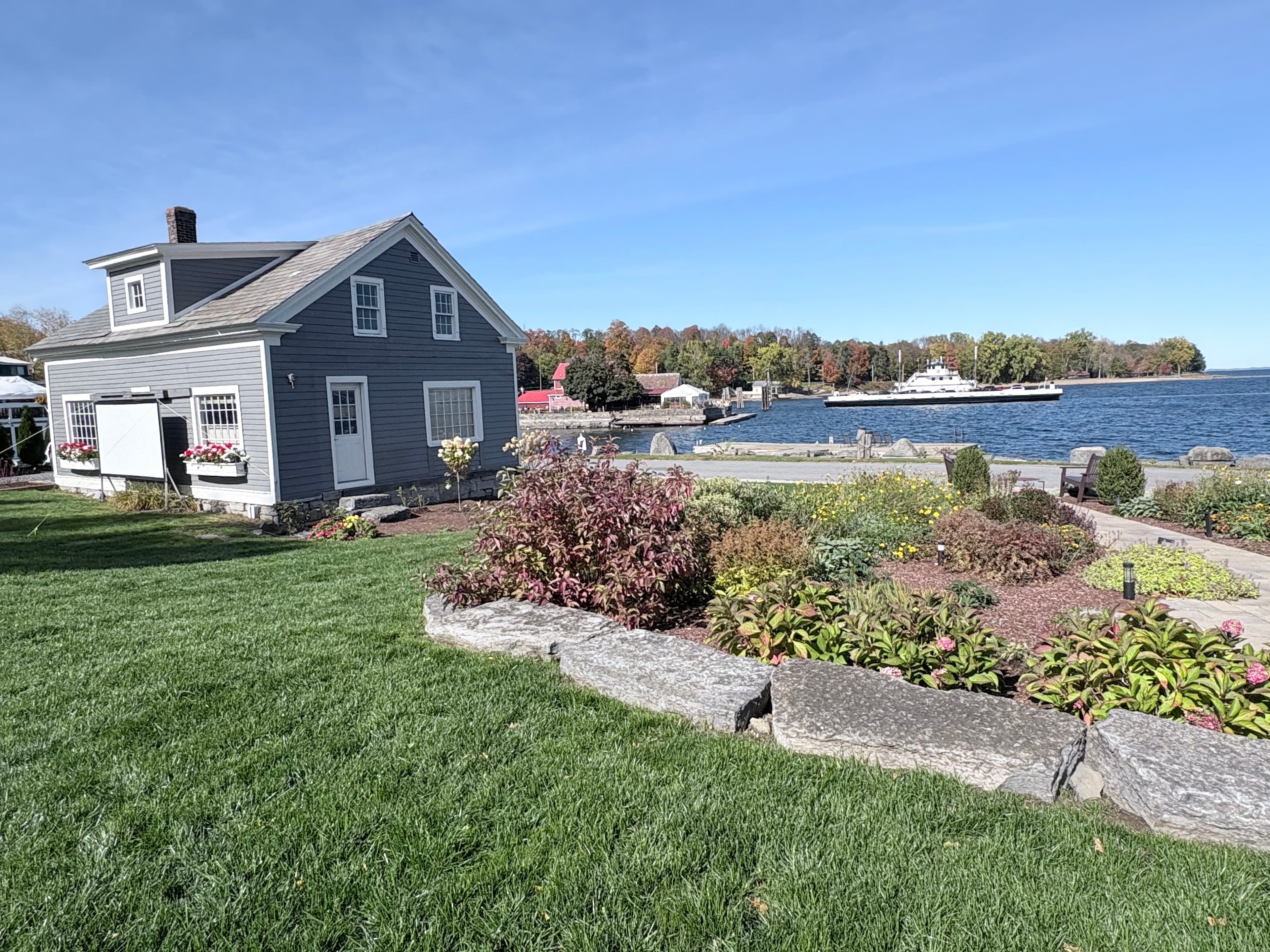 A charming gray house beside a landscaped garden overlooks a tranquil waterway.